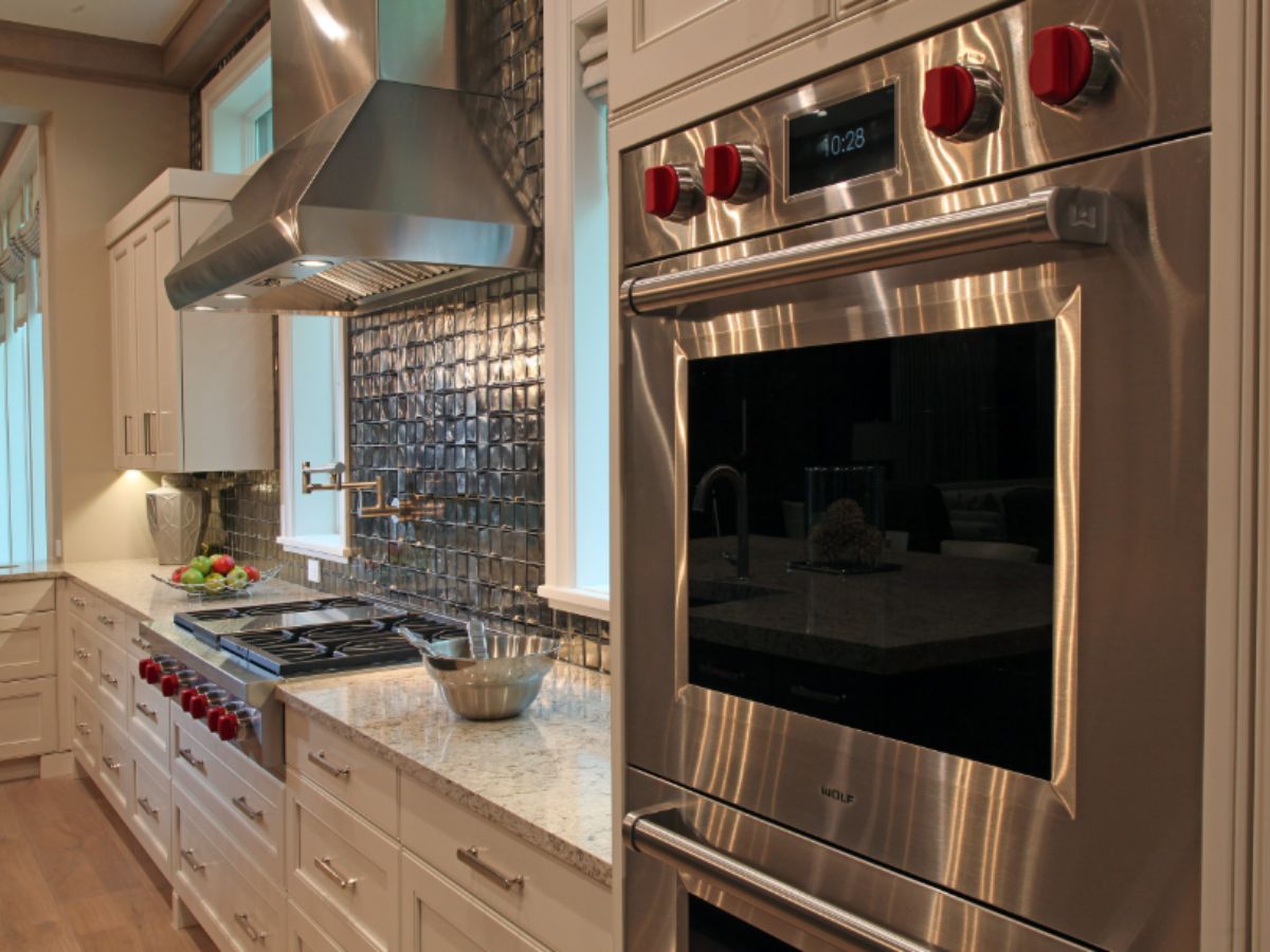 Luxury kitchen cabinets Longboat Key — white recessed panel cabinetry with Wolf wall oven, Wolf range, metallic tile backsplash, and granite countertops by EuroTech Cabinetry